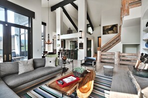 A spacious living area with a grey sofa, a coffee table with a book and remote controls, a wooden side table, and a striped rug.