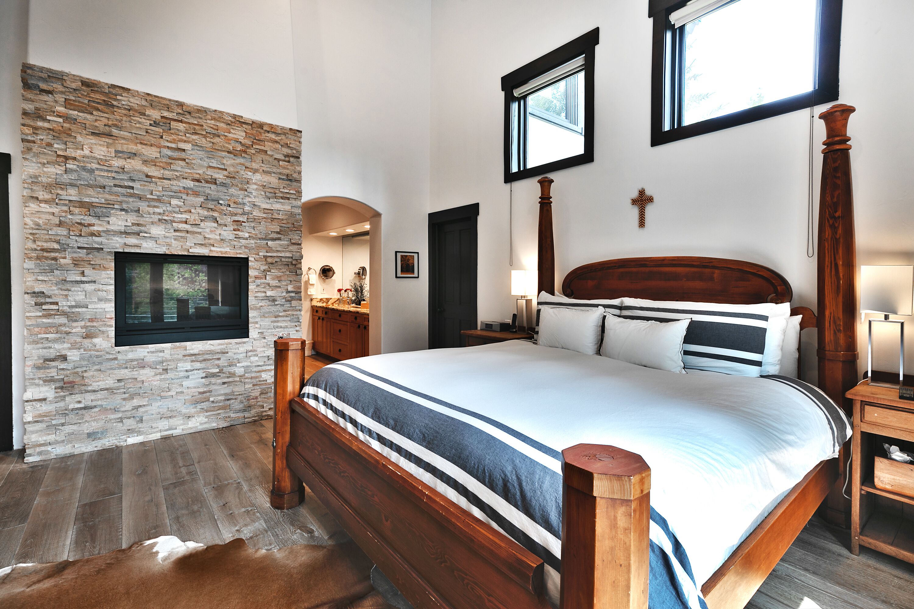 Una camera da letto con parete in pietra, un letto di legno, un comodino, una lampada e una croce appesa al muro.