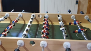 Een tafelvoetbaltafel met meerdere stangen en figuurtjes, geplaatst op een houten oppervlak met een groen speelveld.