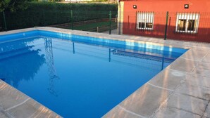 Een rechthoekig zwembad met helderblauw water, omringd door een stenen terras en een metalen hek.