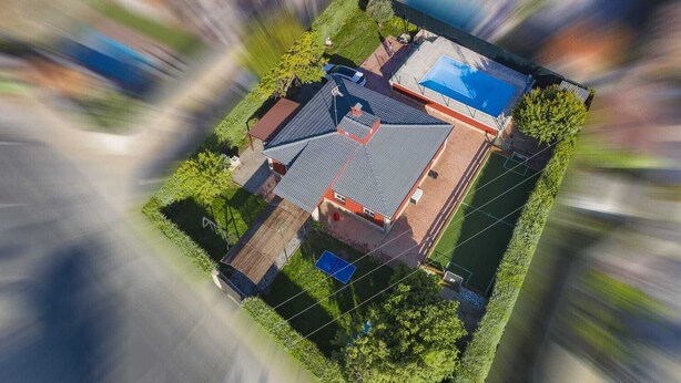 Luchtbeeld van een huis met een zwembad, een tennisbaan en een omheind gazon.