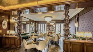 A spacious dining area with high ceilings, ornate columns, and a chandelier. Tables are arranged around a central green seating area. - Hotel-restaurant Erbprinz (Ettlingen)