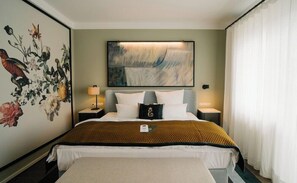Une chambre d’hôtel avec un lit, deux tables de chevet, un tableau accroché au mur et une grande fenêtre avec des rideaux.