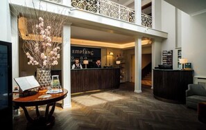 A hotel lobby with a reception desk, a staircase, and a large vase with flowers. - Hotel-restaurant Erbprinz (Ettlingen)