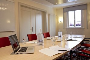 Een vergaderruimte met een lange tafel, rode stoelen, een laptop, documenten en een waterdispenser.