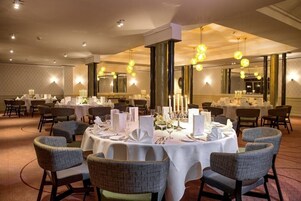 Un comedor con mesas redondas, sillas y centros de mesa con velas.