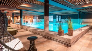 A swimming pool with a tiled floor, a large pillar, wicker baskets with plants, and a chair. - Hotel-restaurant Erbprinz (Ettlingen)