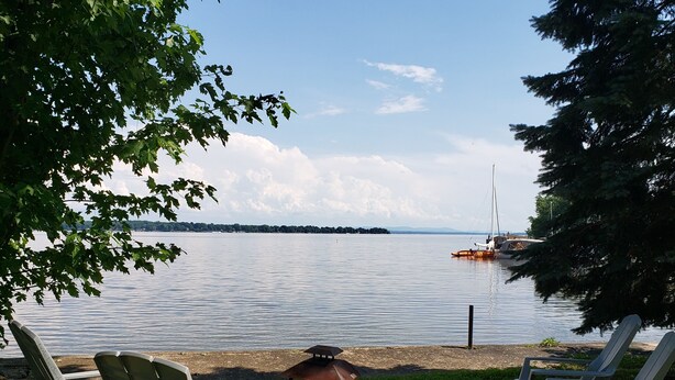 Blick auf einen See mit zwei Liegestühlen und einem Grill.