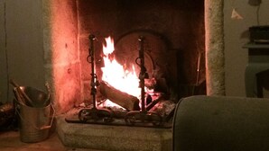 Ein Kamin aus Stein mit Feuer, ein Metall-Eimer und ein Kerzenhalter auf der Kaminbank.