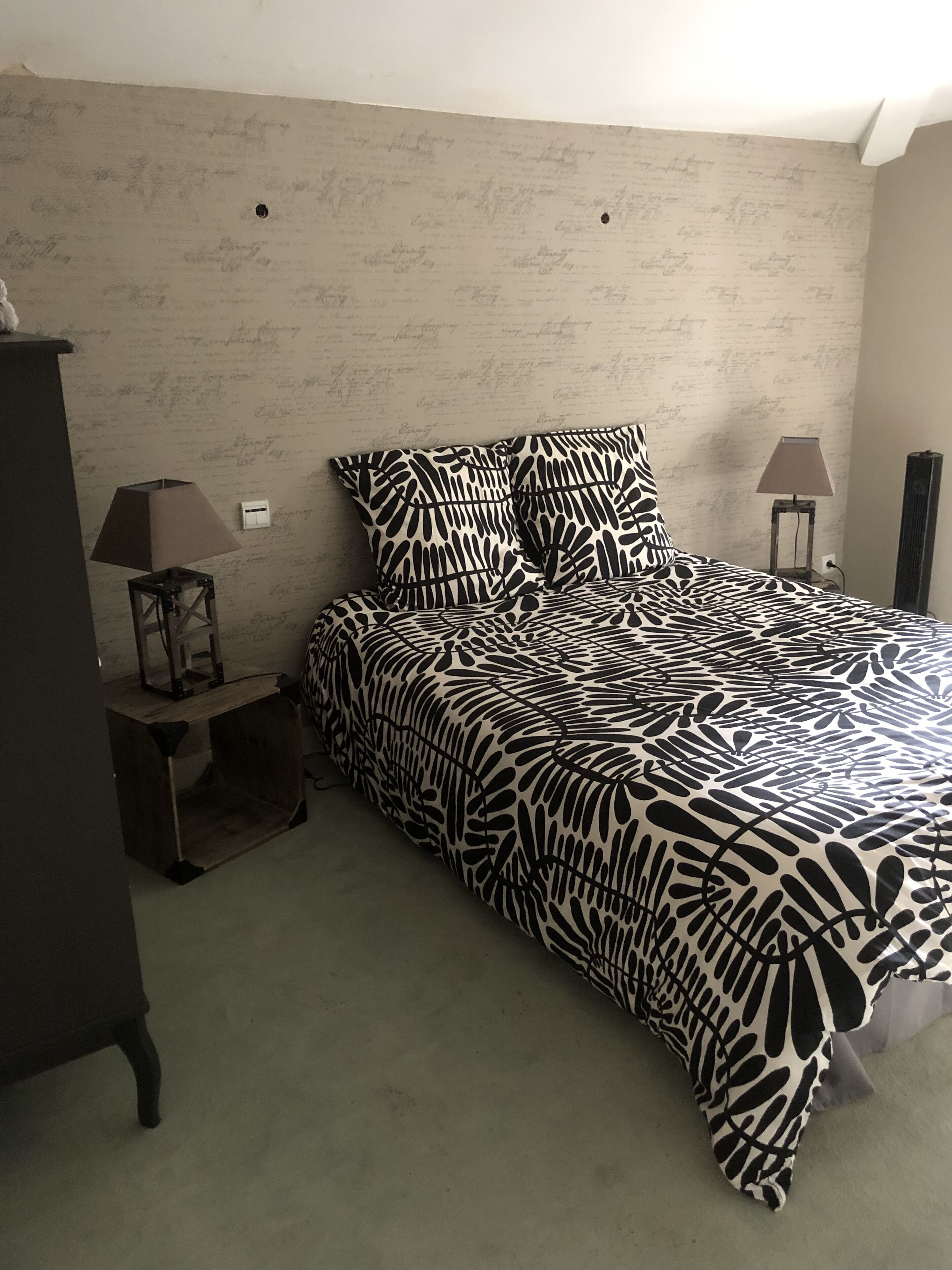 Ein Schlafzimmer mit einem Bett, zwei Nachttischen mit Lampen, einer Kommode und einer Wand mit Muster.