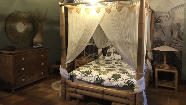 Ein Bett mit Baldachin, eine Holzkommode, ein Spiegel und ein kleiner Tisch mit einer Lampe.