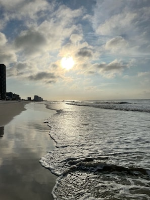Ein Strand mit ruhiger See, blauem Himmel und Gebäuden im Hintergrund.
