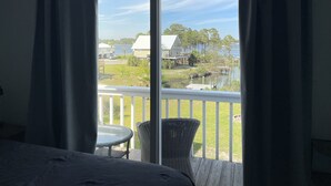 A room with a large sliding glass door leading to a balcony with a wicker chair and a small table. - Updated house on lagoon! Quick walk to the beach and beautiful water view! (Gulf Shores)