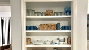 A white shelving unit with glass jars, blue mugs, and woven baskets. - Updated house on lagoon! Quick walk to the beach and beautiful water view! (Gulf Shores)