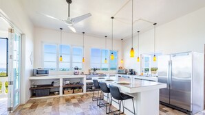 Een moderne keuken met een centraal eiland, een paar barkrukken, een roestvrijstalen koelkast en grote ramen met uitzicht.