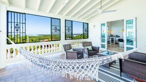 Een ruim balkon met een hangmat, rieten meubels en uitzicht op de oceaan.