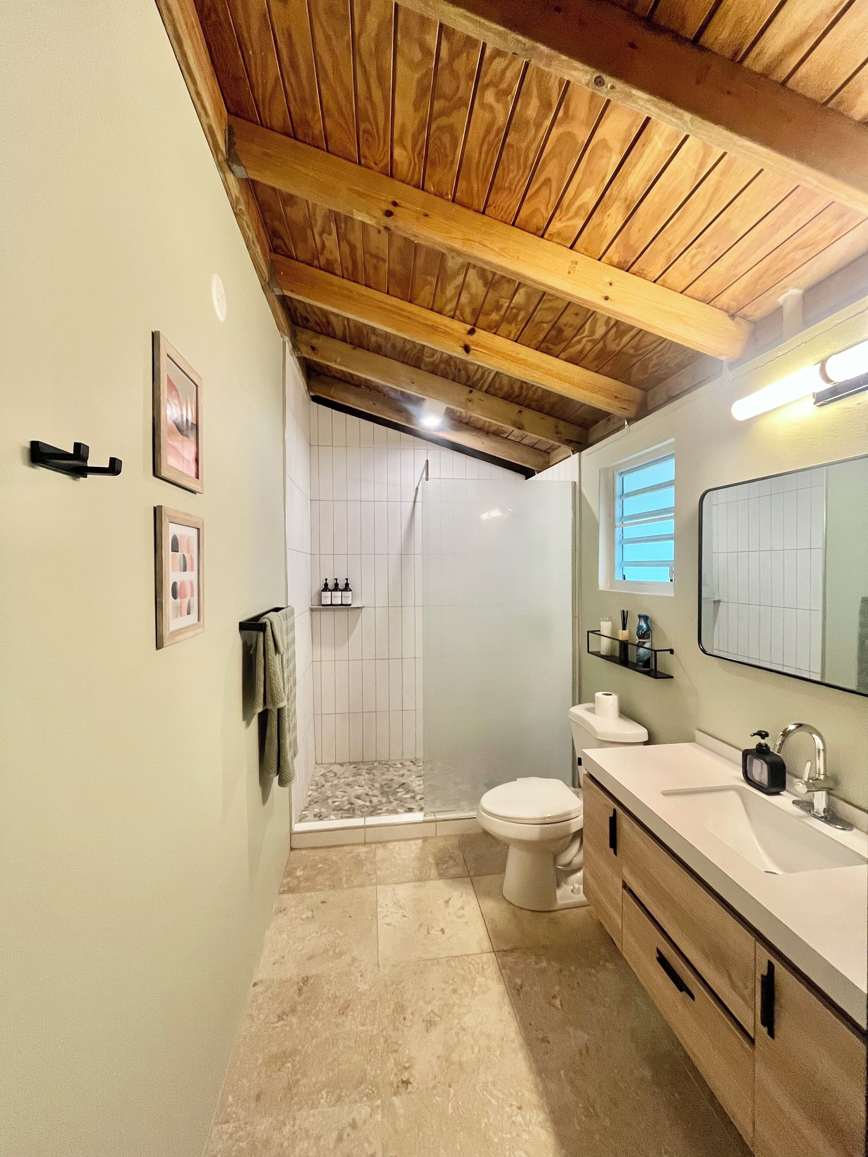 Un bagno con soffitto in legno, una doccia, un water e un lavandino con specchio.