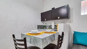 Une cuisine compacte avec un plan de travail en marbre, deux chaises, un petit évier et un meuble sombre au-dessus.