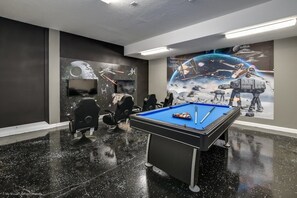 Une pièce équipée d’une table de billard, de chaises et ornée d’une fresque murale sur le thème de l’espace.