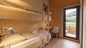 A wooden room with a bunk bed, a desk, a chair, and a large sliding glass door leading to an outdoor area.