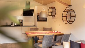 A modern kitchen with a dining area, featuring a wooden table, grey upholstered chairs, and a red table runner.