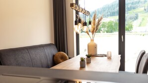 Een moderne eetruimte met een houten tafel, een zwarte gewatteerde bank en uitzicht op een groen landschap door een groot raam.