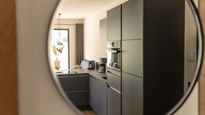 Een moderne keuken met donkere kastjes, een koffiezetapparaat en uitzicht door een rond raam.