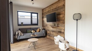 Een moderne woonkamer met een grijze bank, een ronde salontafel en een televisie bevestigd aan een houten wand.