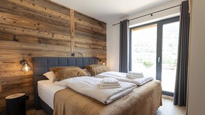 Un dormitorio moderno con una pared de madera, una cama grande con ropa de cama blanca y vistas a través de un ventanal.