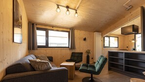 Un interior de madera acogedor con un sofá, sillas, una mesita y una zona de cocina.