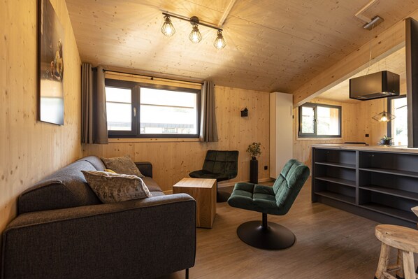 A cozy wooden interior with a sofa, chairs, a small table, and a kitchen area.