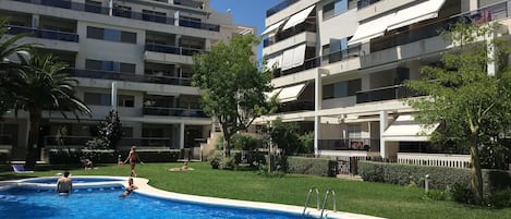 A swimming pool surrounded by a well-maintained lawn, with multi-story residential buildings in the background.