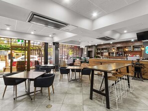 L’intérieur d’un café moderne, avec des tables, des chaises, un comptoir et de grandes fenêtres.