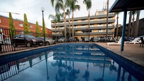 A swimming pool with a clear view of the surrounding buildings, including a multi-story structure with balconies and palm trees. - Breakfree North Adelaide (North Adelaide)