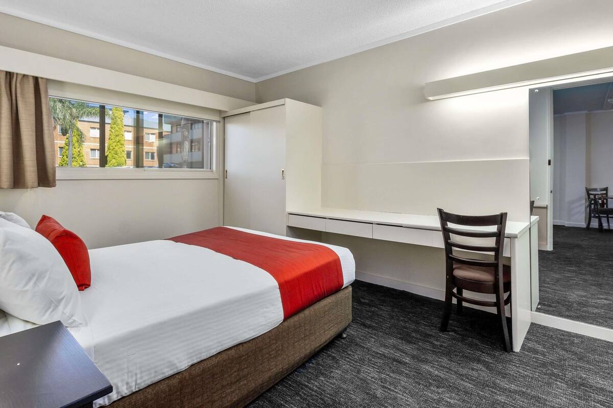 Una camera d'hotel con un letto, una scrivania, una sedia, un armadio e una finestra vista edifici e alberi.