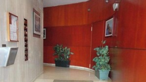 A hallway with a red wall, a reception desk, and two potted plants.