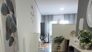 A hallway with a wooden floor, a white sofa, a patterned rug, and a plant.