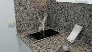 A small kitchen with a granite countertop, a stainless steel sink, a faucet, a roll of paper towels, and a metal dish rack.