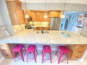 A kitchen with granite countertops, stainless steel appliances, wooden cabinets, and pink bar stools.
