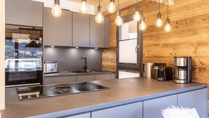 A modern kitchen with a central island, stainless steel appliances, and exposed wooden beams.