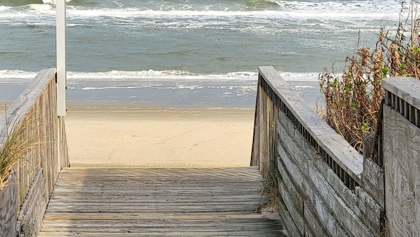 Een houten looppad dat naar een strand leidt, met een bordje waarop 'SHAD' staat.