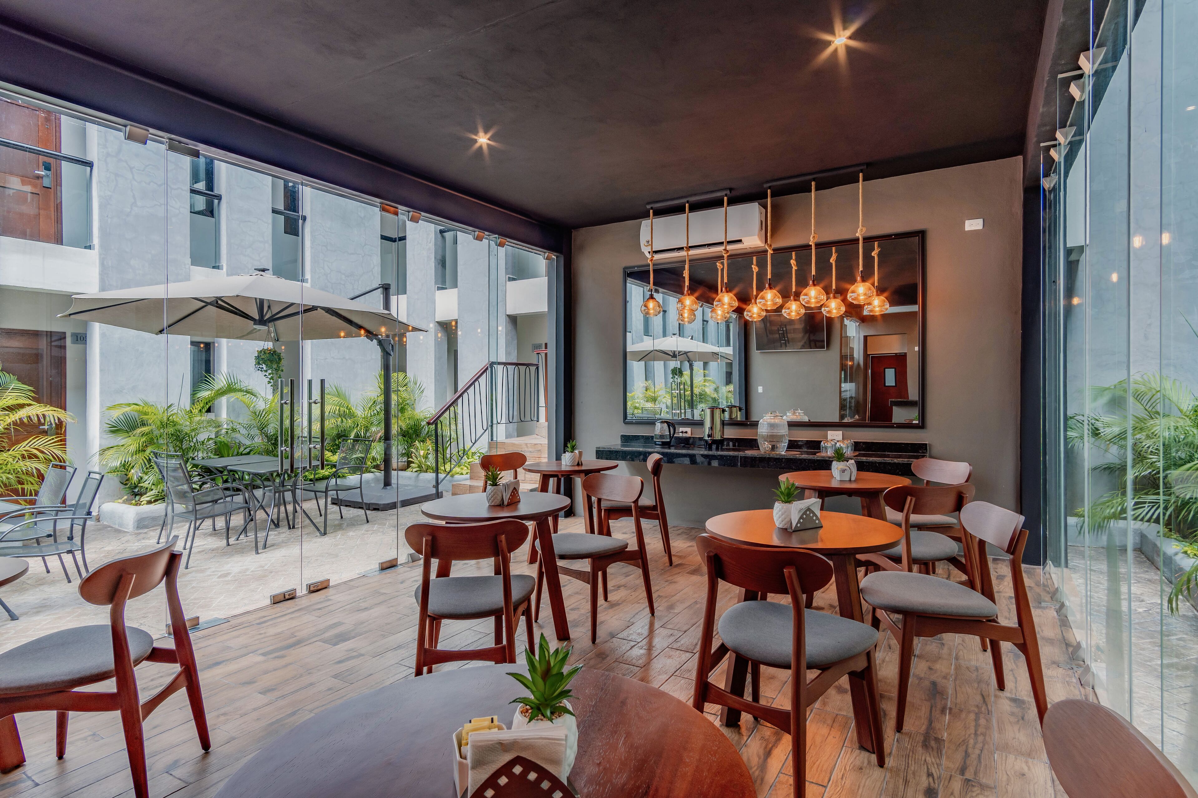 A modern outdoor dining area with wooden tables and chairs, large umbrellas, and hanging pendant lights.