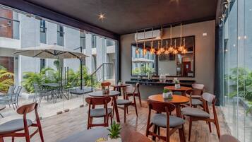 A modern outdoor dining area with wooden tables and chairs, large umbrellas, and hanging pendant lights.