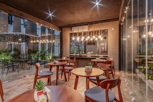 Un restaurante moderno con mesas redondas y sillas de madera, ventanas amplias y lámparas colgantes.