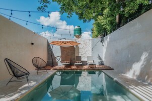 Un área de piscina con sillones de descanso, una sombrilla y luces colgantes.