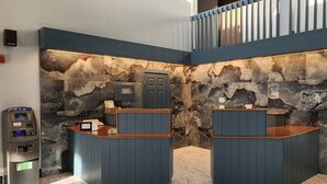 A reception area with two counters, a marble wall, an ATM, and a staircase. - The Oasis Hotel & Bar (Sheboygan Falls)