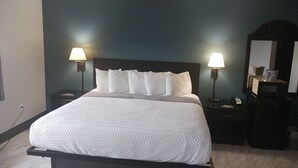 A neatly made bed with white bedding, two bedside lamps, a dark headboard, and a small bedside table with a phone and a lamp. - The Oasis Hotel & Bar (Sheboygan Falls)