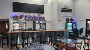 A bar area with a long counter, multiple stools, and a selection of beverages. - The Oasis Hotel & Bar (Sheboygan Falls)