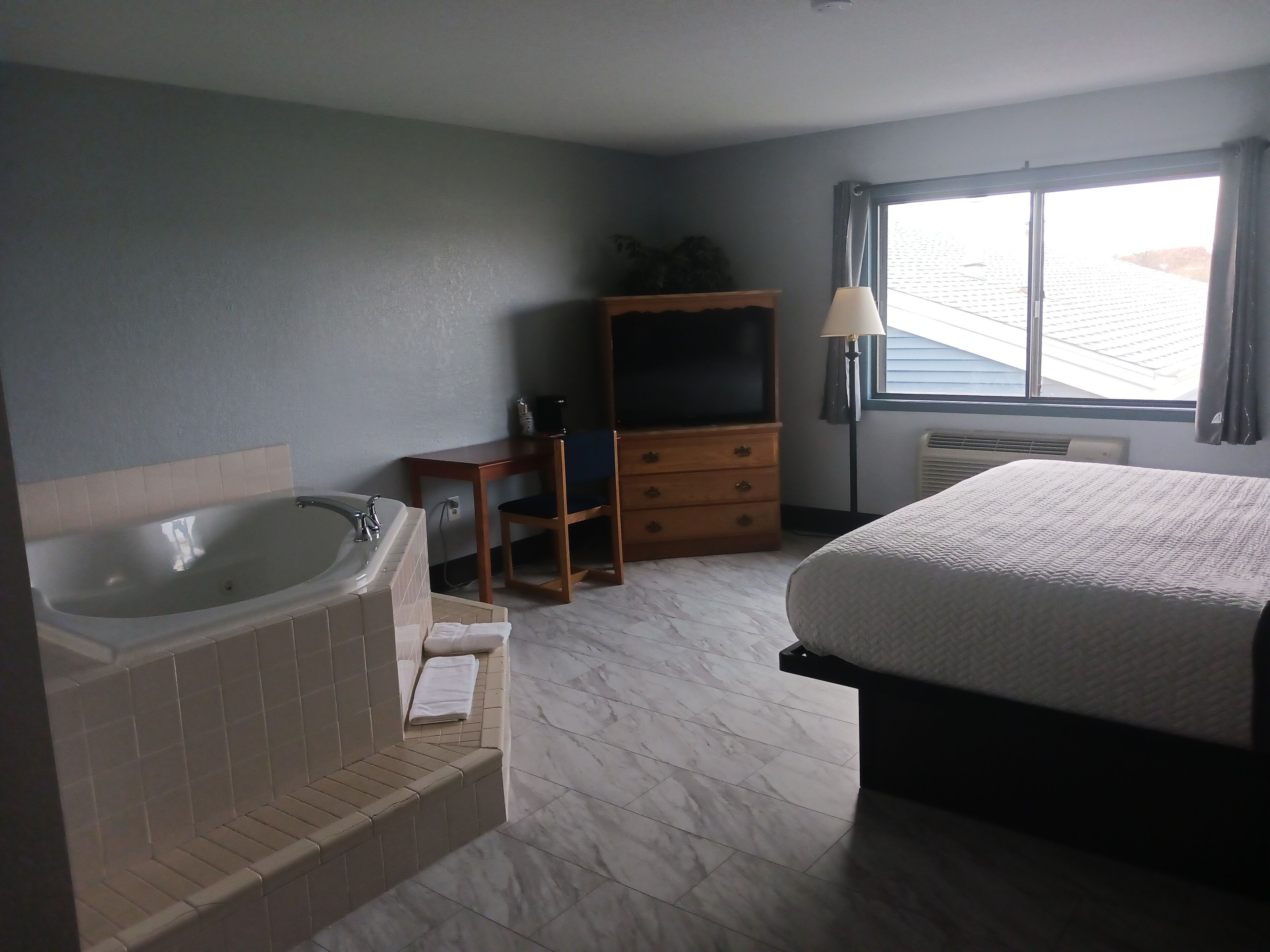 Une chambre d’hôtel avec un grand lit, une baignoire, une commode en bois et une fenêtre avec des rideaux.