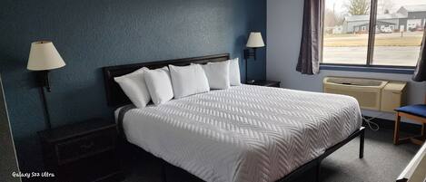 A hotel room with a bed, two wall-mounted lamps, a window with a view of the outside, and a heater.